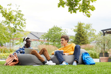 Wall Mural - Full length portrait of two international students chilling on bean bags outdoors in college campus, copy space