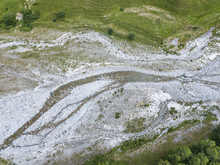 Stony River Bed In High Summer Season Surrounded By Green Alpine Grassland
