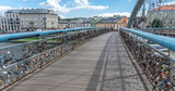 Fototapeta  - Horizontal perspective of the numerous padlocks in the Kładka Ojca Bernatka bridge in Poland, Krakow, with two blurred people walking in the background near an orange building.