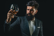 © Volodymyr - Degustation of elite alcohol. Confident bearded man in black suit with glass of cognac. Man with beard holds glass of brandy.