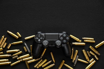 Wall Mural - Modern black gamepad on a black background among the spent cartridges. Game concept. Shooter game.