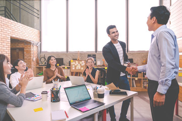 Candid of Indian creative design man smiling and shaking hands with coworker man or colleague and other clapping hand at office workplace. Introduction to team or marketing group concept soft tone.