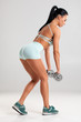 © nikolas_jkd - Fitness woman doing exercise for glutes on gray background. Athletic woman workout with dumbbells