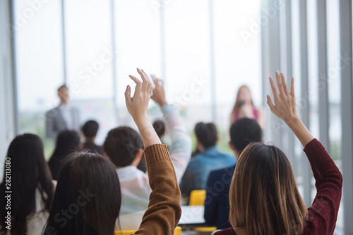 Fotografía Raised up hands and arms of large group in seminar class room to agree with spea