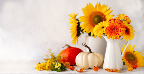 Beautiful autumn still life with bouquet of red and yellow flowers in white vases and white and orange pumpkins on wooden table, front view. Autumn concept with pumpkins and flowers.