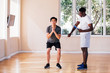 © twinsterphoto - Asian young sportsman doing squat exercise while African American personal trainer watching in gym on summer day