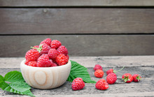 Raspberries In A Bowl Surrounded By Green Leaves On A Wooden Background