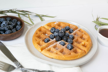 Wall Mural - Belgian Waffle with Blueberries and Maple Syrup, Dusted with Powdered Sugar, Flay Lay on White Background, Copy Space