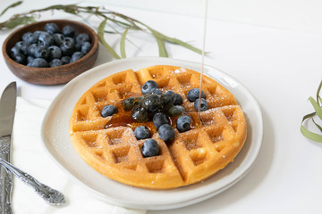 Wall Mural - Maple Syrup pouring on Belgian waffle with blueberries, Dusted with Powdered Sugar, White Background, Copy Space