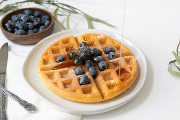 Wall Mural - Maple Syrup pouring on Belgian waffle with blueberries, Dusted with Powdered Sugar, White Background, Copy Space