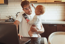 Multitasking Father Working From Home On Laptop With Baby Daughter