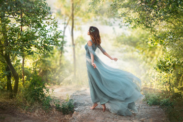 fairy-tale princess in light summer blue turquoise dress on wide path and walks towards wind, gracef