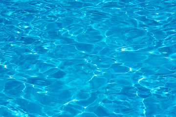 background of water in a blue swimming pool, water surface with sun reflection