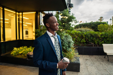 African American businessman wearing blue suit drinks coffee near office. Business concept