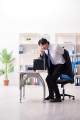 Young male employee in the office in time management concept