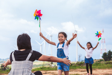 Wall Mural - Two asian child girls playing with wind turbine toy and running to their mother to give a hug in the wind turbine field