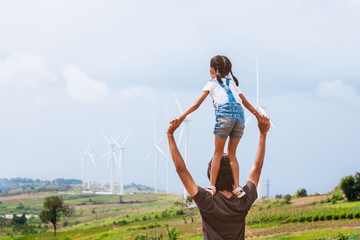 Wall Mural - Father and daughter having fun to play together. Asian child girl riding on father's shoulders in the wind turbine field