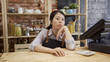 © PRPicturesProduction - Beautiful Asian pensive barista woman in apron leaning on bar counter in coffee shop. bored lady coffeehouse staff waiting for customer in modern style cafe store. startup small business concept.