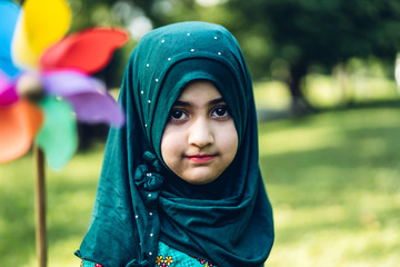 Portrait of happy little muslim girls child with hijab dress smiling and looking at camera in the park