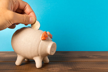 A man's hand putting a coin in a piggy Bank. The concept of saving money.