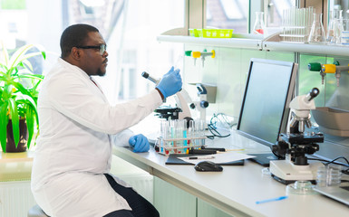 African-american scientist working in lab. Doctor making microbiology research. Laboratory tools: microscope, test tubes, equipment. Biotechnology, chemistry, bacteriology, virology and health care.