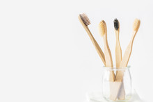 Charcoal wooden bamboo toothbrushes in glass cup on white background. Zero waste plastic free eco friendly reusable materials for teeth hygiene health. Poster banner