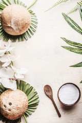 Wall Mural - Wooden bowl with coconut oil and spoon on light background with coconuts, tropical leaves and flowers. Natural organic  concept. Top view.  Vegan coconut butter. Vegan ingredients. Healthy lifestyle