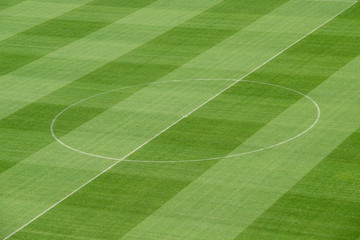 Freshly mowed green grass on the football - soccer field with center lines in the middle.