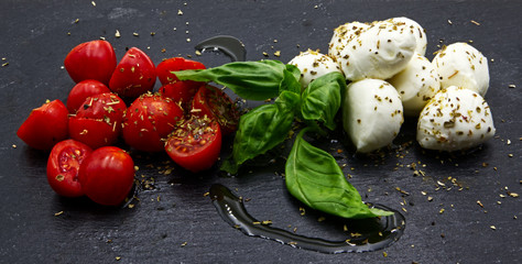 Mozzarella and tomatoes on black slate. Oil, origan and parsley