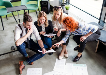 A group of young business people sitting on the floor in an office, talking.