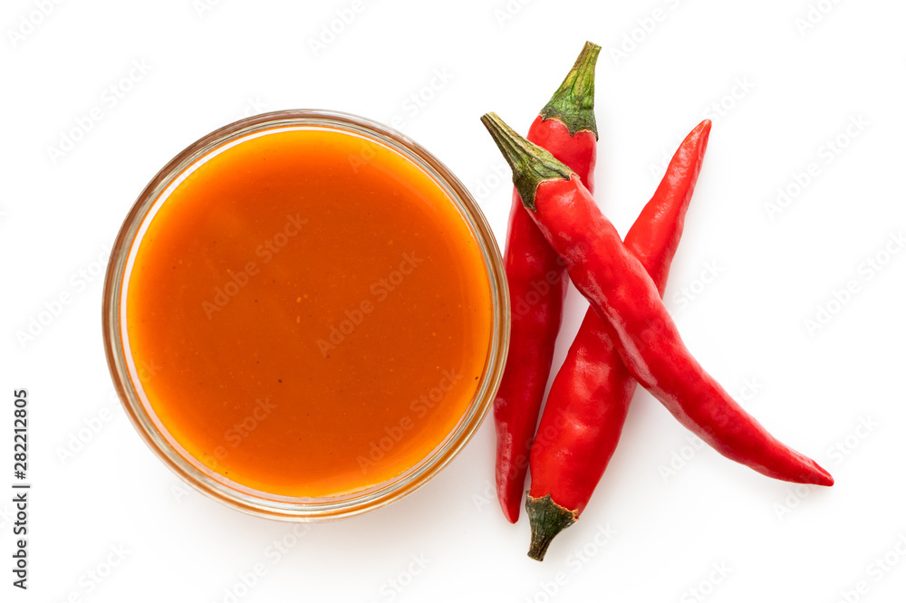 Peri peri chilli sauce in a glass bowl next to three red chillies ...