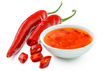 Sweet chilli sauce in a white ceramic bowl next to one whole and one cut red chilli isolated on white.