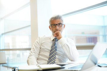 Wall Mural - Portrait of mature businessman sitting at desk looking into camera