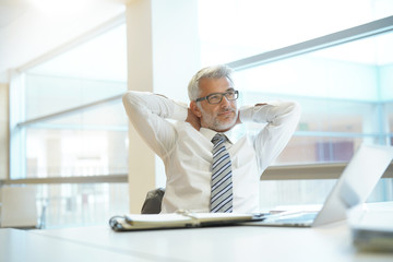 Poster - Relaxed businessman sitting at desk with arms behind head