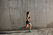 © Liubov Levytska - Jogging, endurance and sport concept. Side shot fit sporty young woman in activewear running near concrete wall into sun, daily training and morning exercises, sportswoman training to run marathon