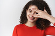 © Cookie Studio - Wellbeing, happiness and tenderness concept. Attractive hispanic young girl dark curly hairstyle cover eye silly look through fingers look amused tender gentle grin, standing white background