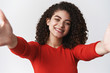 © Cookie Studio - Close-up caring lively charismatic girl dark curly hairstyle stretch hands forward hold camera taking selfie smiling delighted posting personal photograph, standing white background hugging