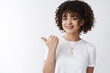 © Cookie Studio - Try this. Friendly-looking happy smiling relaxed stylish curly woman white t-shirt pointing thumb left showing excellent copy space promo product grinning suggesting check-out, recommend