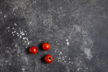 A bunch of ripe cherry tomatoes on a dark background of marble, coarse salt on delicious red tomatoes. Copy space, concept minimalism.