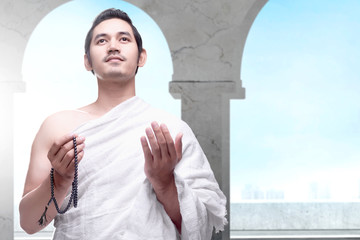 Sticker - Asian Muslim man in ihram clothes standing and praying with prayer beads while raised arms