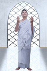 Wall Mural - Asian Muslim man in ihram clothes standing and praying while raised arms