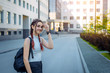 © exebiche - Young beautiful student with backpack on her shoulder goes to school, close-up. Schoolgirl with two braids standing in front of college, blurred background. September 1, the beginning of school year.