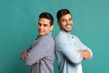 Two Latin Guys Standing Back-To-Back On Turquoise Studio Background