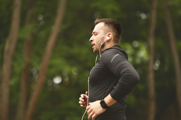 Wall Mural - Young male athlete in earphones jogging in park