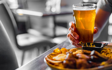 Wall Mural - man hand with glass of cold beer and plate with snacks on wooden table background on bar or pub