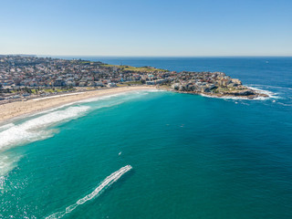 Wall Mural - Beautiful aerial high angle drone view of the suburbs of Bondi Beach and North Bondi, one of the most famous beaches in Sydney, New South Wales, Australia. Motor boat driving through the ocean.