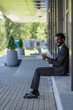 © LIGHTFIELD STUDIOS - cheerful african american businessman smiling at camera while sitting on parapet and holding newspaper
