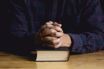 Wall Mural - Hands of praying young man and Bible on a wooden table.
