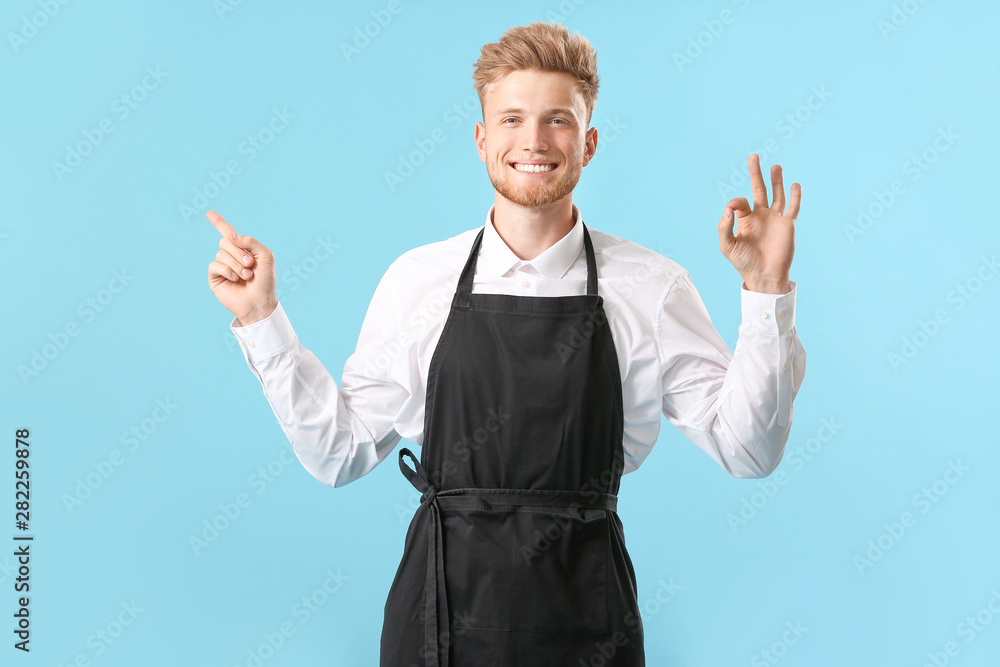 Handsome male chef pointing at something and showing OK on color background