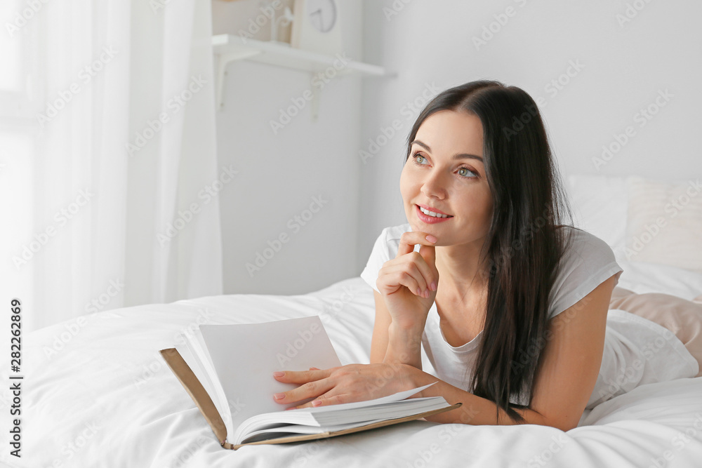 Beautiful young woman reading book in bedroom
